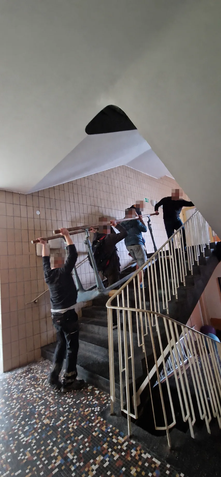 Anonymisiertes ONT-Team beim Transport eines sperrigen Bauteils im Treppenhaus